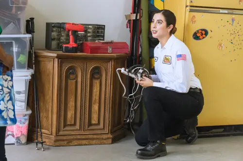 Jane, a Sarasota Mister Sparky electrician, working in a garage and holding electrical tools while assisting a customer.