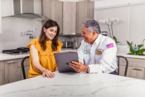 Mike, a Sarasota Mister Sparky electrician, consulting with a homeowner at the kitchen table using a tablet.