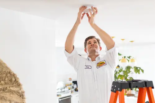 Pete, a Sarasota Mister Sparky electrician, installing a smoke detector on a ceiling in a residential home. What Smoke Detectors Do Firefighters Recommend?
